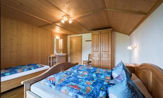 A cozy room with wooden walls and two beds. The bedding is colorful and designed with a maritime theme.