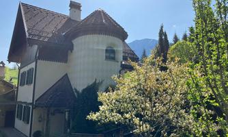A charming house with a unique roof and colorful windows. In the foreground, trees are blooming against a clear blue sky.