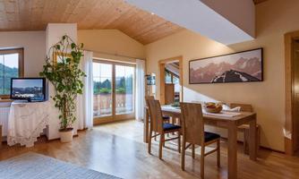 A cozy living space with wooden floors and large windows. A dining table with chairs and a plant give the room an inviting atmosphere.