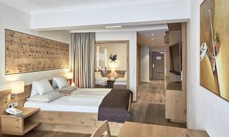 A bright hotel room with wood paneling, two beds, and a table. The decor is modern and inviting, with a large window and art on the wall.