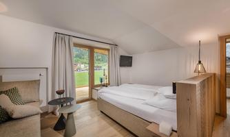 A modern bedroom with a cozy bed and a window view of nature. The room is bright and friendly with wood and textile accents.