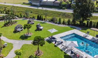 A beautiful garden with a swimming pool and sun umbrellas. You can see comfortable loungers and some people in the water.