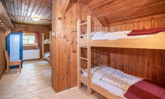 A cozy sleeping room with wooden paneling and bunk beds. The room has large windows and a blue wardrobe.