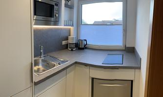 A modern kitchen with white cabinets and gray countertops. It features a window, a sink, a microwave, and a dishwasher.