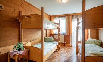 A cozy sleeping area with wooden bunk beds. The sun shines through the windows, creating a bright, inviting atmosphere.