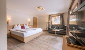 A modern hotel room with a large bed and a cozy seating area. The bright walls and wood design create an inviting atmosphere.