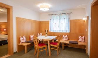 A cozy room with a table and chairs. Wooden paneling is on the walls and bright curtains are present.