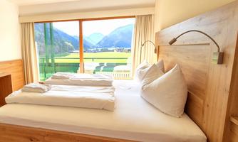 A cozy bedroom with a large window and a view of the mountains. The bed is inviting with white pillows and blankets.