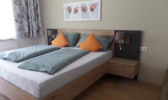 A cozy bedroom with a double bed and orange pillows. The walls are light and decorated with a modern picture.