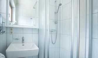 A modern bathroom with a shower and a sink. The walls are tiled in light colors and there is a window.