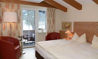 A cozy hotel room with a double bed and red armchairs. Large windows offer a view of the snowy landscape outside.