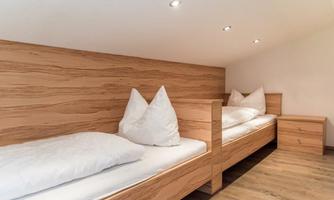 A cozy bedroom with two wooden beds and white pillows. The walls are made of light wood, and there is soft ceiling lighting.
