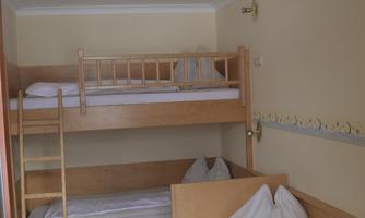 A simple room with a bunk bed and a single bed. The furniture is made of light wood and the room is bright and cheerful.