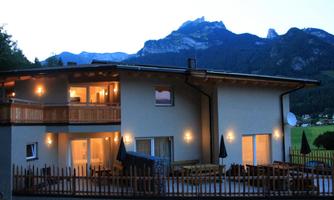 A modern house at the foot of the mountains with illuminated windows. The surroundings are quiet and offer a beautiful view of nature.