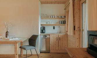 A modern wooden kitchen interior with a table and a chair. The kitchen is bright and well-equipped with dishes and appliances.