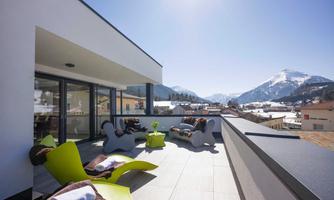 A modern rooftop terrace with cozy seating areas. In the background, snow-covered mountains and a clear sky can be seen.