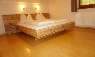 A modern bedroom with a double bed made of wood. The room is bright and friendly, with warm light.