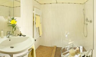 A modern bathroom with a shower and a sink. On the sink, there is a vase with a flower and decorative accessories.
