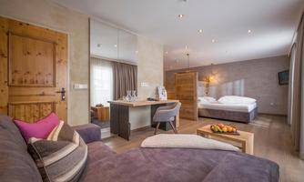 A modern hotel room with a large bed and a seating area. The decor is cozy and features wooden details.
