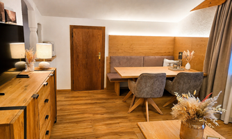 A cozy dining area with wooden interior and a large table. The warm atmosphere is enhanced by soft lighting and decorative elements.