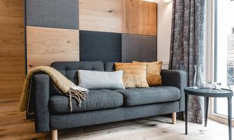 A modern living room with a gray sofa, colorful cushions, and wood paneling.  
Large windows let in plenty of light and create a bright atmosphere.