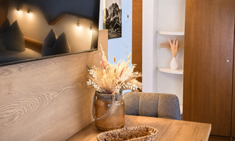 A cozy dining area with a wooden table and a decorative flower vase. The room has warm colors and modern elements.