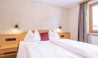 A cozy room with two single beds and bright pillows. Large window with natural light and simple wooden details.