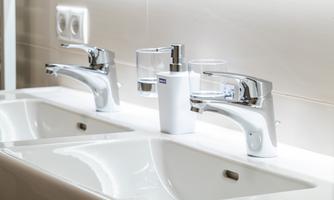 Two bathroom sinks with modern, shiny fixtures. Between the sinks is a soap dispenser.