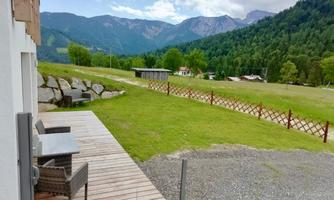 A peaceful landscape with a meadow, trees, and mountains in the background. On the terrace, there are garden furniture inviting you to relax.