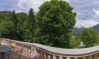 A beautiful terrace with a view of green trees and the mountains. The sky is partly cloudy and the scenery is calm and peaceful.
