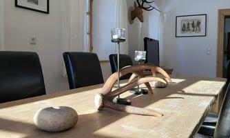 A dining room with a long wooden table and black chairs. On the table are a stone and a antler as well as candle holders.