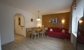 A cozy living room with a red sofa and a dining table. The walls are bright, and there is soft lighting.