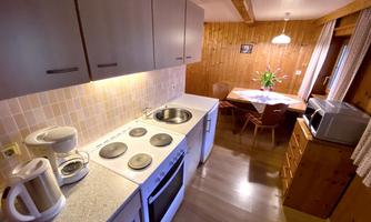 A bright kitchen with modern appliances and wooden paneling. In the background, there is a dining table with flowers in a vase.
