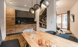 A modern dining room with a wooden table and stylish chairs. The kitchen is well-equipped and there is a nice view of a balcony.