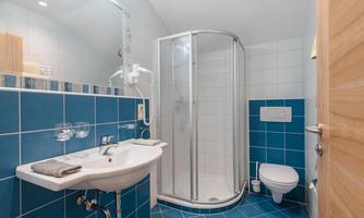 A modern bathroom with blue tiles and a shower. There is a sink and a toilet in a bright, clean room.
