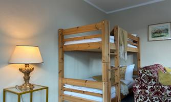 A cozy room with a wooden bunk bed. Next to the bed is a lamp and a beautiful armchair.