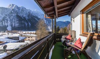 A balcony with a view of snow-capped mountains. Cozy chairs and cushions invite you to relax.