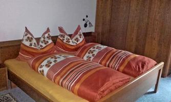 A cozy bedroom with a wooden bed and colorful bedding. The pillows are decoratively stacked and create an inviting atmosphere.