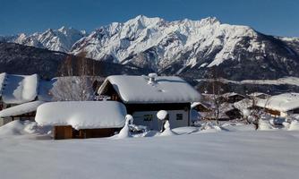 A snowy landscape with a cozy house and majestic mountains in the background. The sky is clear and blue.