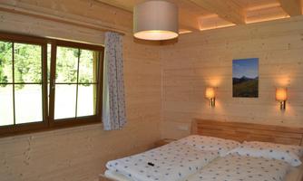 A cozy bedroom with wooden paneling and a large window. The bed is equipped with white blankets and pillows.