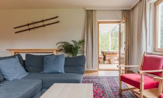 An inviting living room with a gray sofa and a red armchair. Large windows let in plenty of daylight and offer a view outside.