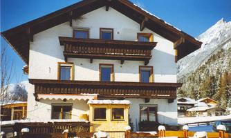 A charming alpine house with three floors and balconies. It is surrounded by snow-capped mountains and offers an inviting atmosphere.