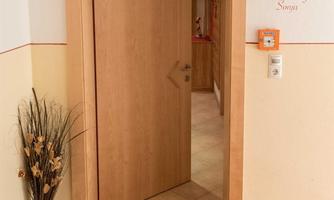 A bright entrance area with an open door. Next to the door is a small plant and useful information is attached to the wall.