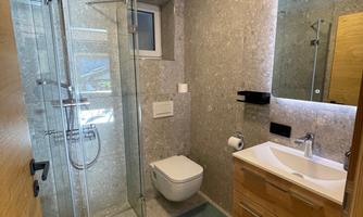 A modern bathroom with a glass shower and wooden details. The walls are painted in neutral colors, and there is a large mirror above the sink.