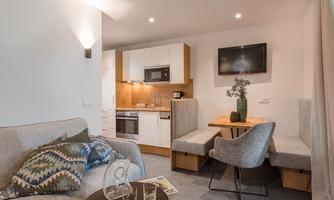 A modern living kitchen with a cozy sofa and a dining table. The kitchen is bright and well-equipped.