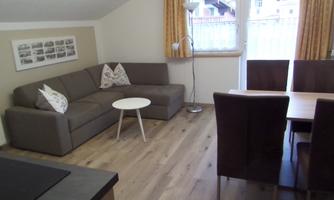 A cozy living room with a gray sofa and a small white table. The dining area is furnished with a wooden table and dark chairs.