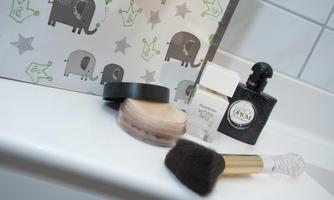 A beautiful makeup table with various cosmetic products, including powder, perfume, and a brush. In the background, there is a decorative bag with elephant motifs.