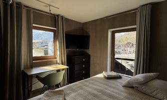 A cozy bedroom with a large bed and a desk. Large windows provide a view of the surroundings.