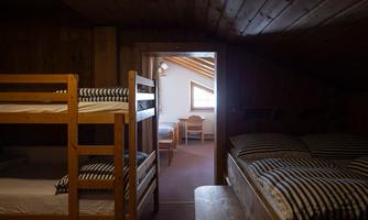 A cozy dormitory with two bunk beds and a single bed. The room has wooden walls and a window that lets in daylight.