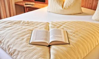 A cozy bed with an open book in the middle. The comforter and pillows are beige and soft.
